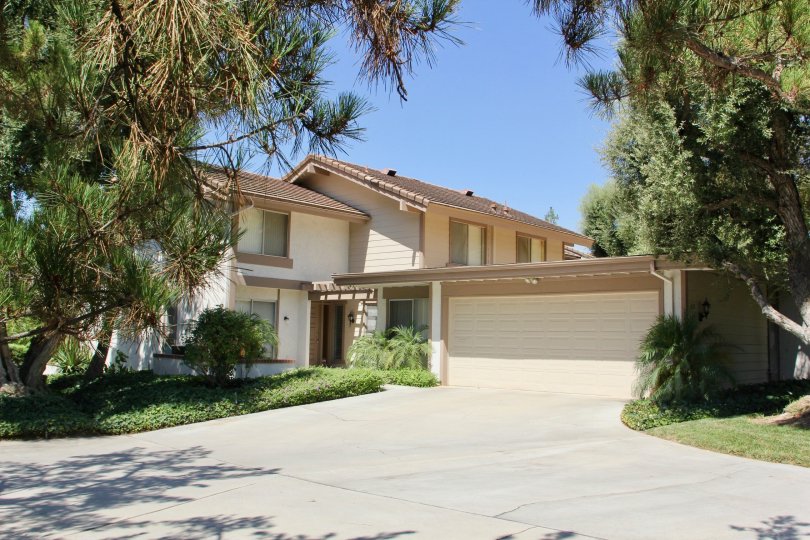 House nested in large trees with garage and manicured lawn and gardens