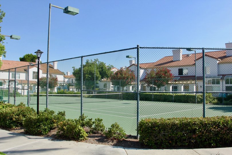 Fenced in tennis court surrounded by white townhomes in Rancho Del Mar