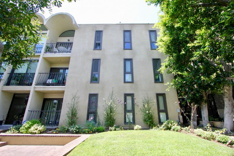 Outside view of three story building with well manicured lawn, lovely flowers and shrubs, and sunny balconies.