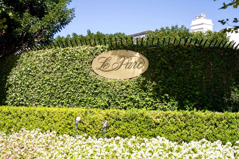 A gold plaque surround by shrubs on a fence display the name Le Parc