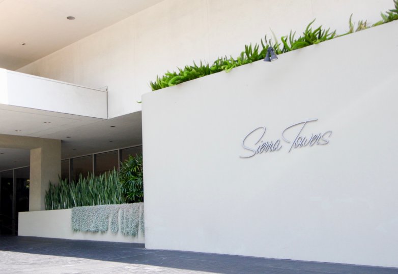 A BOARD THAT REPRESENT A PLACE AND LOOKS LIKE A BUILDING WALL NEAR TO THE PLACE AND SOME PLANTS THERE