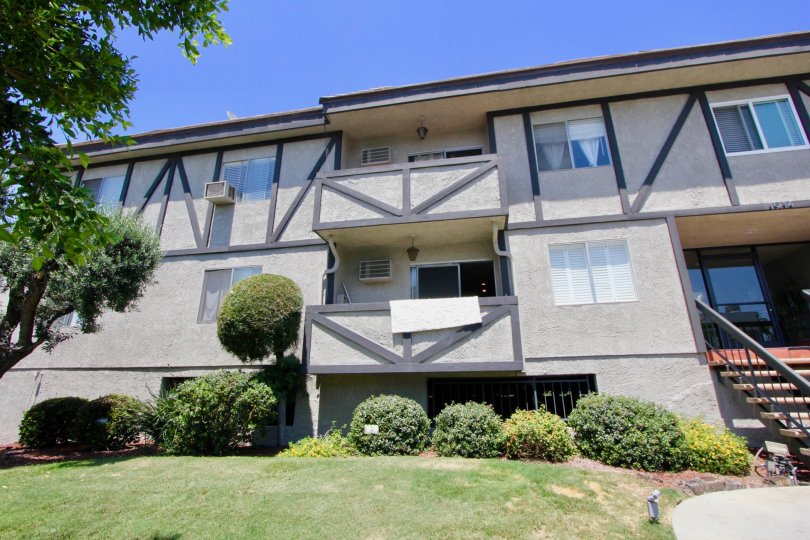 Sunny day at two story 1914 Corinth in West LA, California; front steps and door, towel hanging over first floor balcony. There are trees, grass, and bushes.
