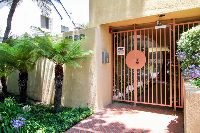 A yellow house at the Walden Condos neighborhood with a red gated fence and small palm trees