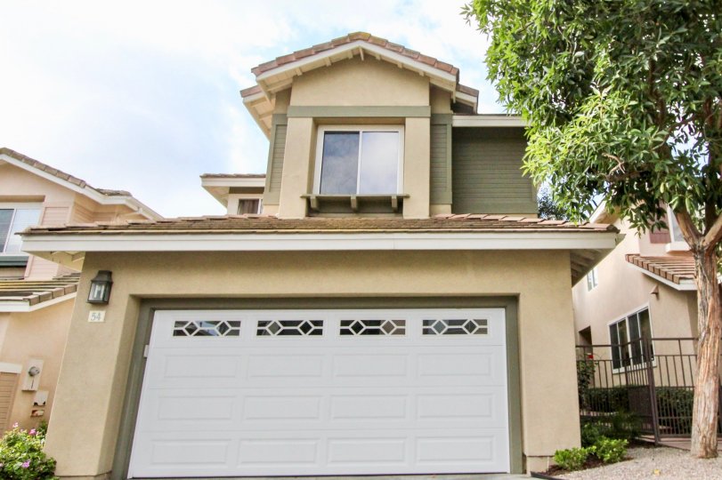2 storey home with double car attached garage, stucco siding and mature tree with decorative car door at the Cottages