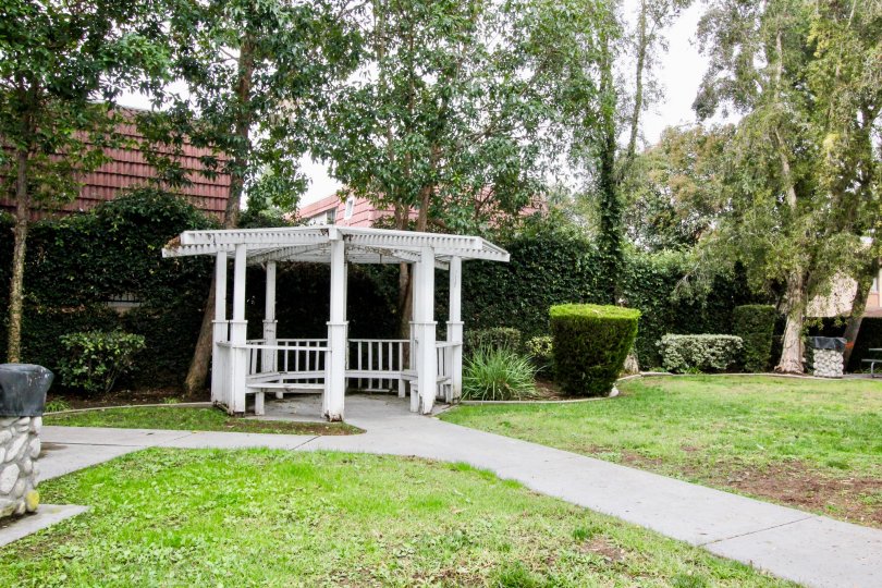 THIS IMAGE SHOWS THE GARDEN WITH RESTING PLACE ON THE PATHWAY, LAWN, LOT OF TREES, PLANTS LOCATED IN BUENA PARK
