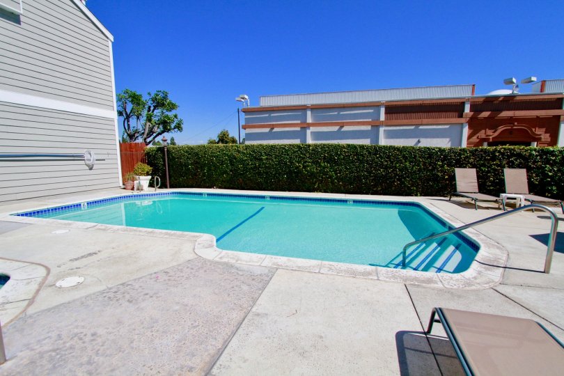 A oddly shaped crystal blue pool with steps and railing at Victoria Garden Villas in Costa Mesa CA