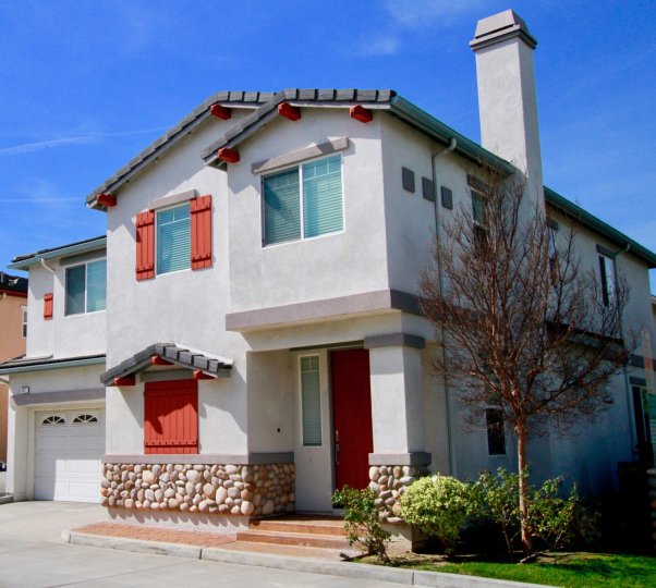A sunny day at the front door of a two-floor house in the Cove community with a few bushes