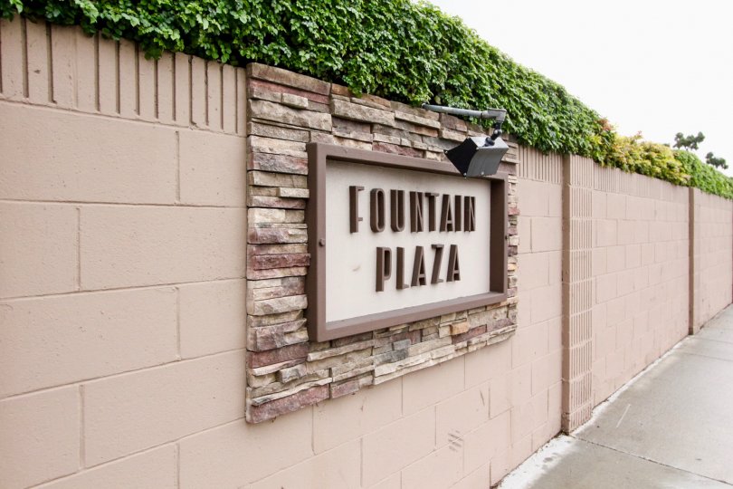 A long tan wall with the sign pictured in tan and brown in the Fountain Plaza community.