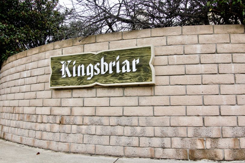 Entrance sign backing made of bricks and the sign is wood and cream lettering showing the community name Kingsbriar.