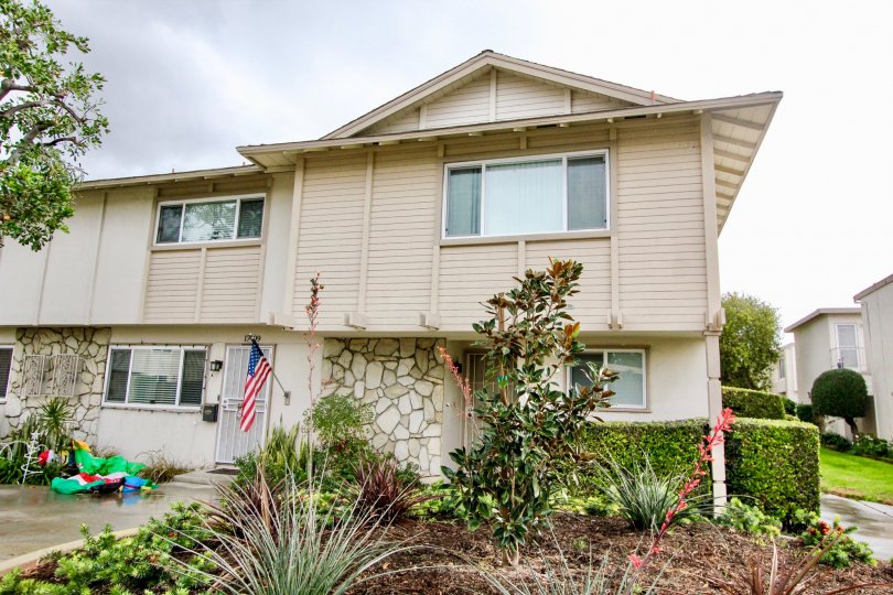A beautiful grey building in the Paradise Manor with a flag, and glass windows, flowering plants near the house.