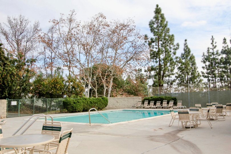 A pool in Case Del Vista with deck chairs and tables on a cloudy day.