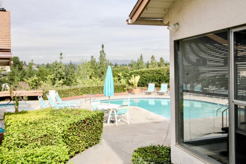 The house with a pool and a dining table also available at the outdoor of the house and a small garden also located near to the pool at the sunshine time.