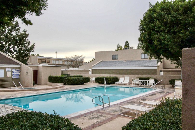 Seating chair, tables and trees are present near the swimming pool in The Arbor