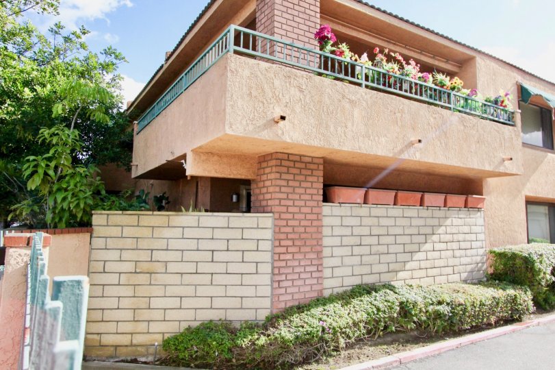 Sunny spring day outside a neighborhood house with brick pillars and cement walls with flowers on the balcony.