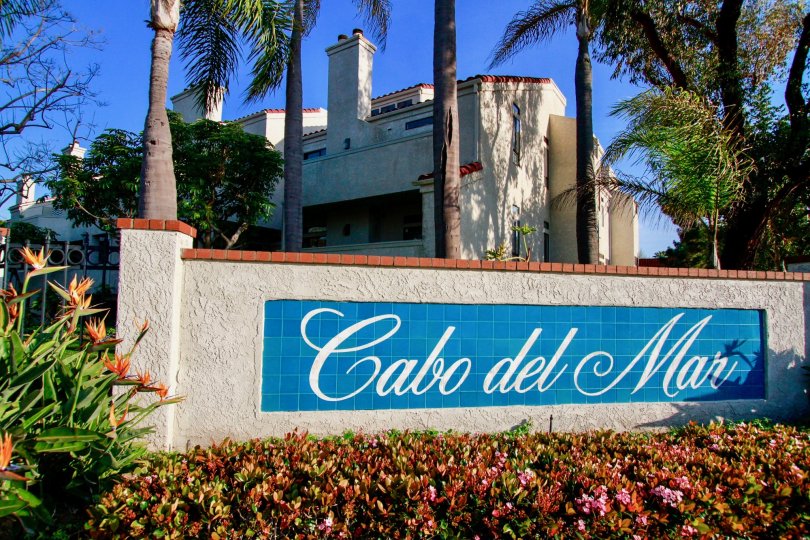 THE BOARD OF SIGN REPRESENTS CABO DEL MAR AND MORE FLOWERS ARE IN FRONT OF THE BOARD AND A BUILDING BACKSIDE OF THE SIGN AND SOME TREES ALSO AVAILABLE.