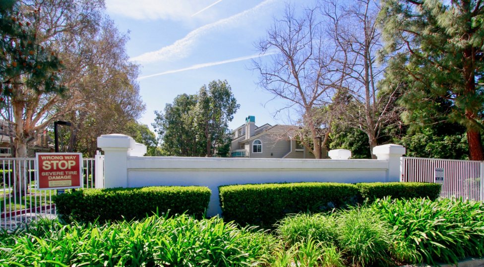Pacific Ranch Villas entrance with a metal gate and bushes on a sunny day.