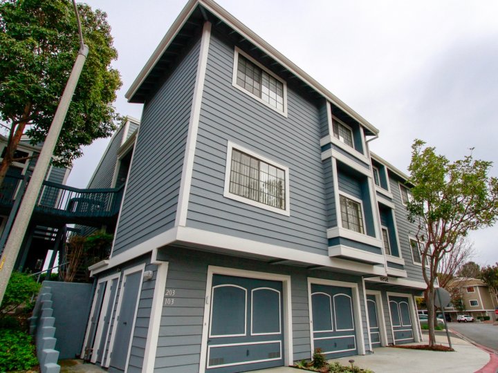 The blue Seabridge Townhomes with bright green tree landscaping and a cement sidewalk entrance.