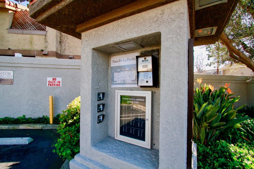A CALLING BOX LOCATED AT A WALL AND A BOARD NEXT OF WALL CONTAIN NO PARKING AND ALSO A SMALL SIGN NEAR TO THE PLACE AND IT LOOKS LIKE A HOUSE WAY.