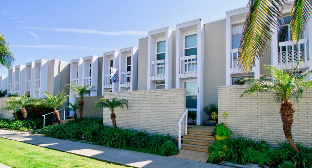 THE APARTMENTS ARE LOOKING BEAUTIFUL WITH WHITE COLOUR AND A SMALL ROAD NEAR TO THE PLACE AND TREES AND PLANTS ALSO NEAR TO THE APARTMENTS.