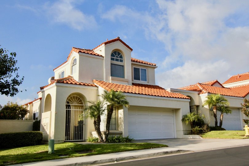 a sunny day in the laguna sur with a house that has the entrance at the left side with a closed parking door in the centre with small trees in front