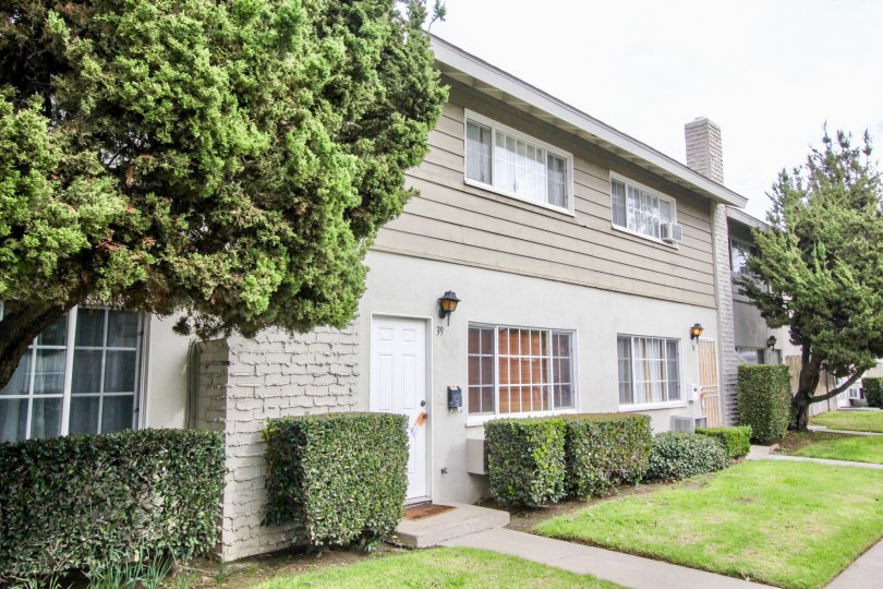 A grey home in The California with bushes and trees on a sunny day