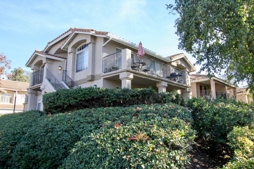 Multi floor house with pillars and wrap around deck with trees and shrubs.