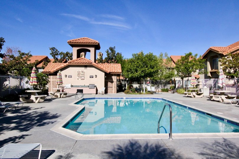 A sunny day by a pool in Vista La Cuesta with tables, umbrellas, and a wholesome landscape all around