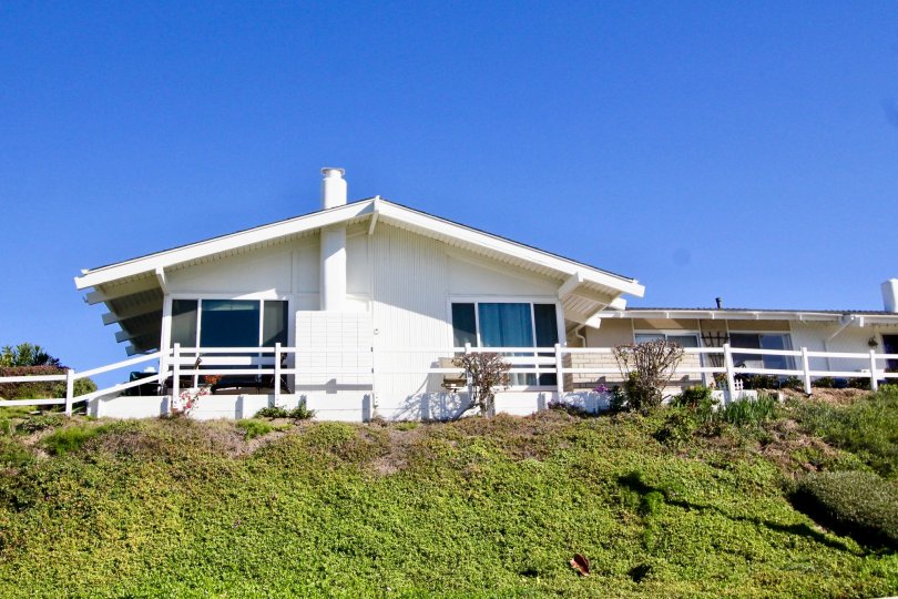 A white wooden fence sits near a house on a hill at Colony Cove