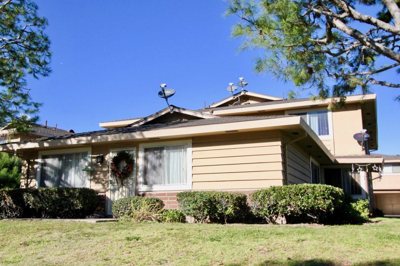 A sunny day at a Casa De Capistrano house with a Christmas wreath on the front door and trees on each side and bushes in front of the house