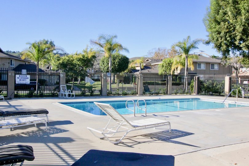 The sparkling blue pool at Casa De Capistrano with pool chairs, tall fencing and palm trees