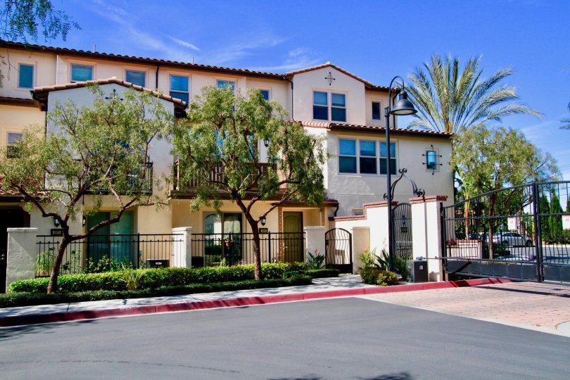 A white condo building of Avenue E with trees and a gate on a sunny day