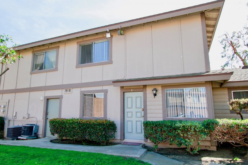 Two story Normandy Place apartment building with white doors and trimmed bushes.