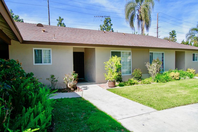 The greay color house in the Saddlebark Park Villas with a beautiful flower garden, trees, green grass and shrubs.