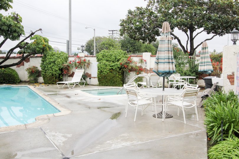 Pool area in the community of Macaw Cove in Tustin, California. Hot tub with lounge chairs and tables with umbrellas nearby,