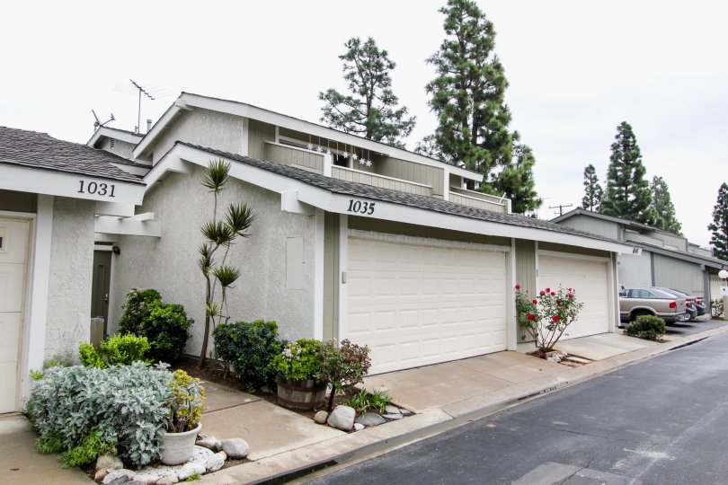 An overcast day by a block of Tustin Pines houses with three cars parked in the driveway at the end and tall trees behind the houses