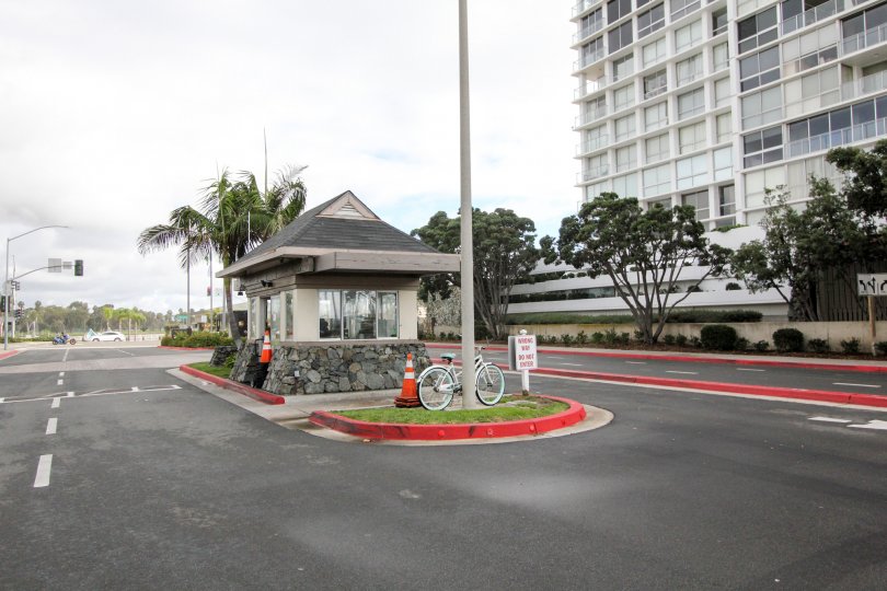 The entrance to a parking lot with a guard cabin, some cones and a bike, and a big building in the back in Coronado Shores, Coronado, CA