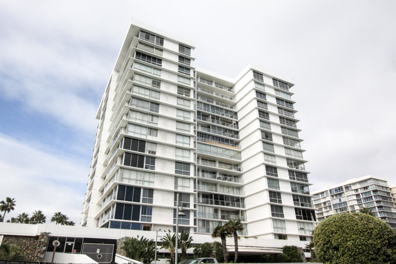 Tall white high rise under clouds with trees at its base at Coronado Shores in Coronado CA