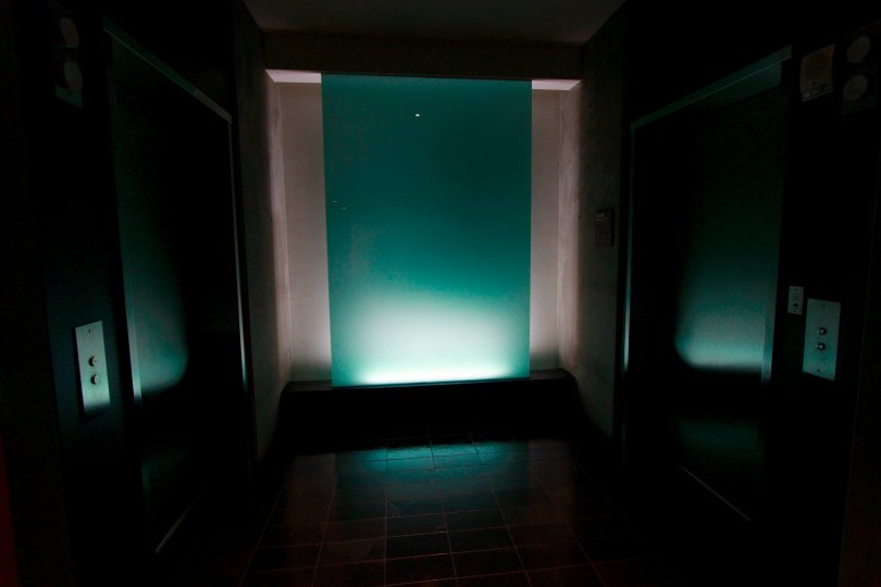 A single light pointed upwards illuminates a teal wall.