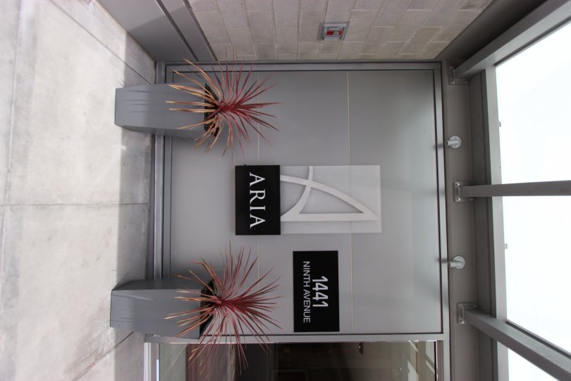 A view of the exterior front of the Aria building with potted plants on ninth avenue.