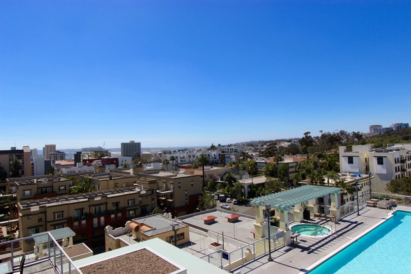 Downtown San Diego building in the Discovery community in California. The view from the roof of a building of a large part of the city and blue sky in the background. Pool and hot tub are pictured on the bottom right.