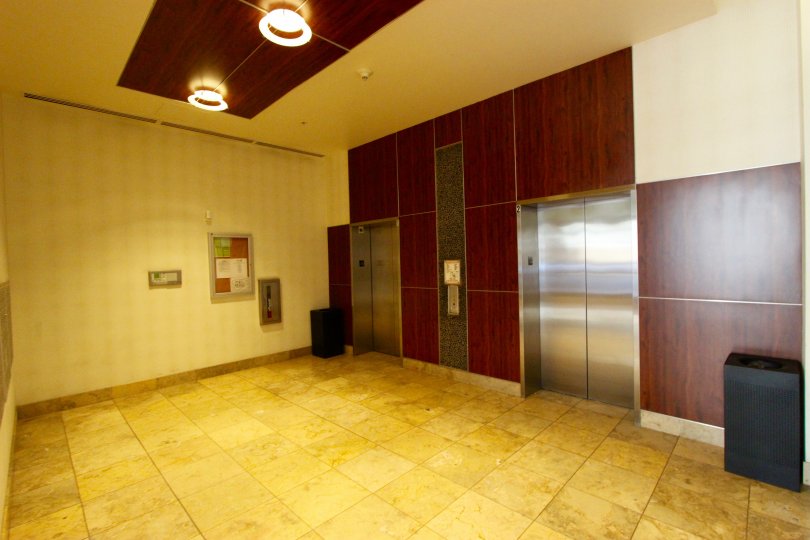 Two silver elevators sit on a wall with wood paneling in Downtown San Diego, CA