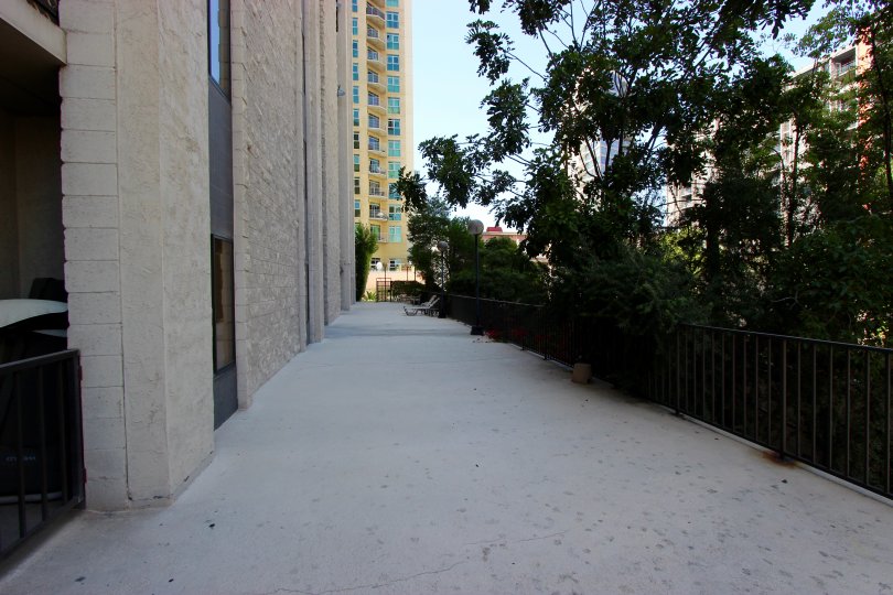 A sunny day in the area of Symphony Terrace, sidewalk, fence, trees, high rise apartments
