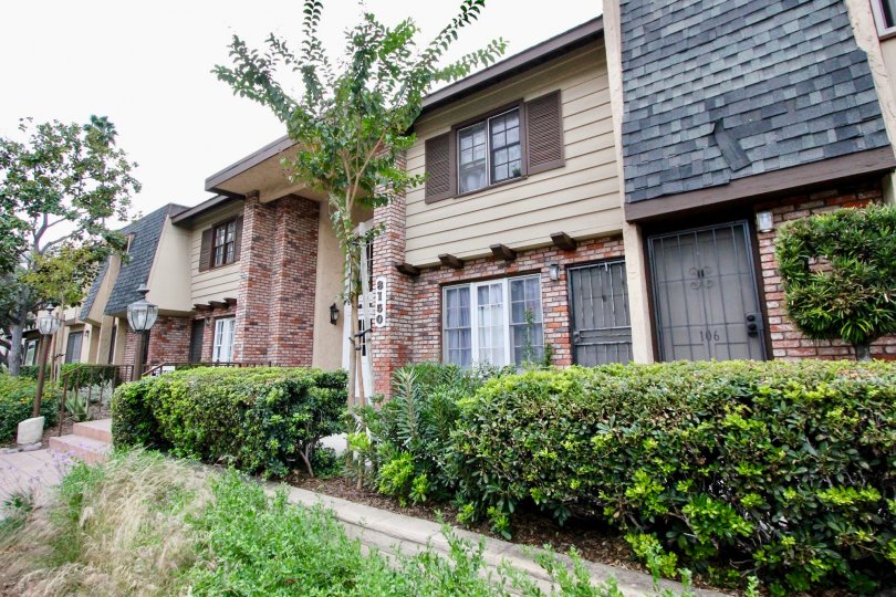 A two story condominiums with gray tiles behind a row of hedges inside La Mesa Village in La Mesa CA