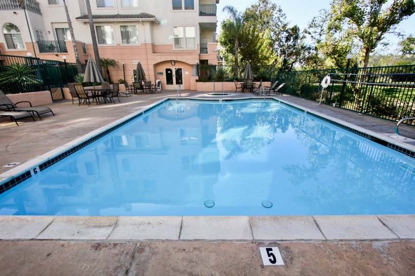 A 5' Deep, sunny inground pool patio area with umbrellas and seating for recreation in River Scene Mission Valley, California.
