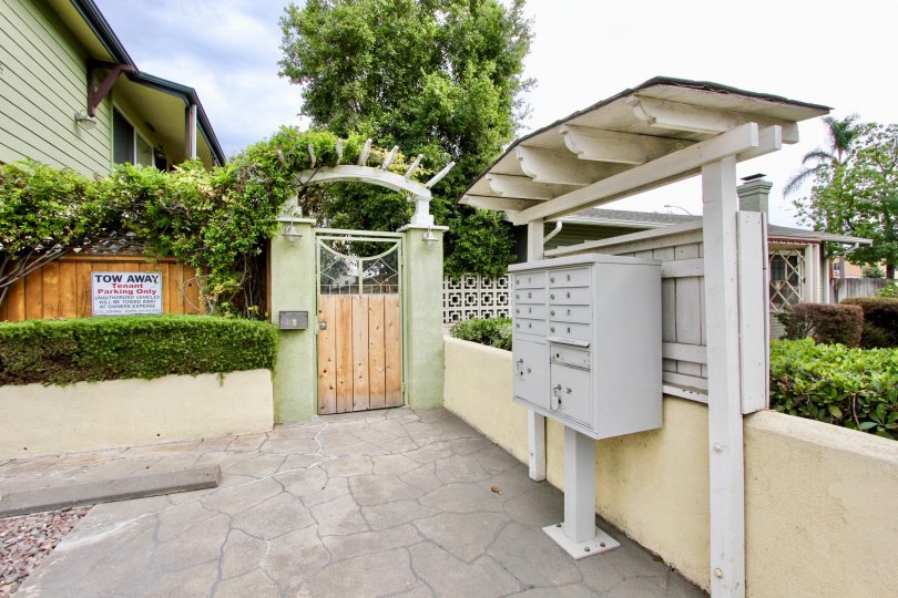 A gray metal mailbox sits under an awning near a gravel parking lot outside of an olive green apartment building in the Magnolia Walk community in North Park California