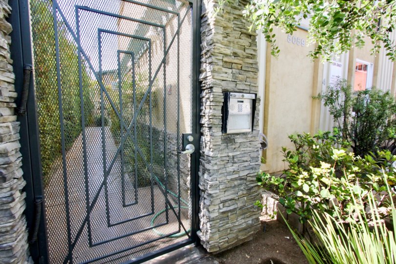 A sunny day at The Beach House, in front of the community gate with an intercom system and near a garden.