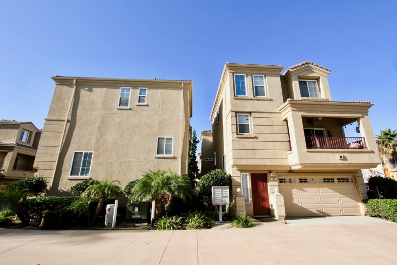 Three story town homes with a large brown garage door next to plants inside Sea Breeze Beach Cottages in Oceanside CA