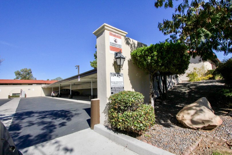 The entrance to a parking lot with a car parked inside and some bushes on the side during a sunny day in Bernardo Villas, Rancho Bernardo, CA
