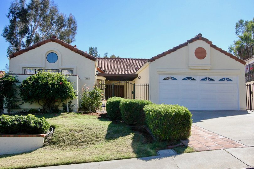 A beige house with a white garage and some bushes in front during a sunny day in Las Brisas, Rancho Bernardo, CA