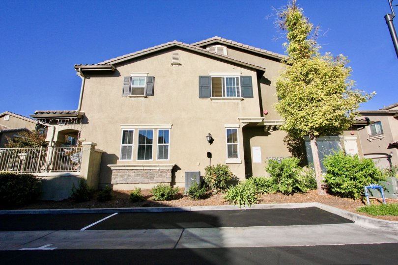 A sandy house with a tree and some bushes in front during a sunny day in Ravenna, Rancho Bernardo, CA